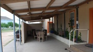 Un patio couvert avec une table et des chaises, une petite marche menant à une porte, et des plantes en pot le long du mur.