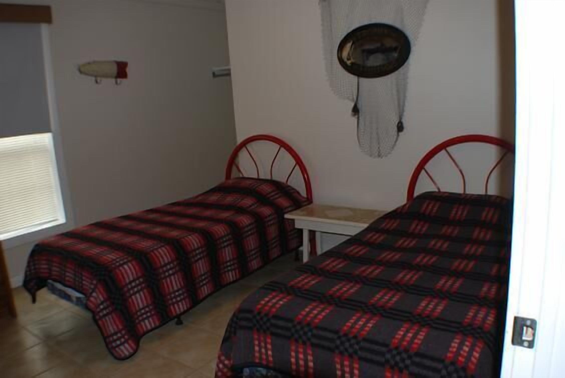 Une chambre avec deux lits simples, une petite table et une étagère fixée au mur.