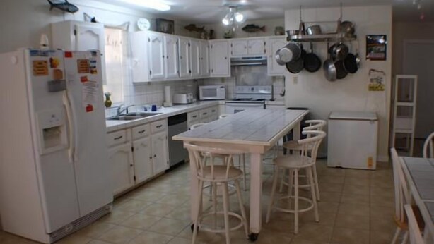 Une cuisine avec des meubles blancs, un îlot central doté de tabourets, un réfrigérateur, un four à micro-ondes et une cuisinière.