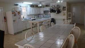 Une cuisine avec des meubles blancs, une table à manger et des chaises. On y trouve un réfrigérateur, un four à micro-ondes et une cuisinière.