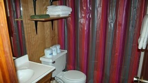 Pieni kylpyhuone, jossa on wc, pesuallas ja hyllyjä hygieniatuotteille.