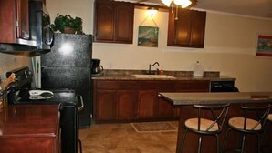 A kitchen with wooden cabinets, a refrigerator, a coffee maker, and a bar stool area. - Knots Landing #2 - Newly remodeled 2 Bedroom/2 Bath (Port Mansfield)