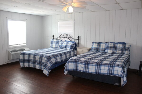 A room with two beds, white walls, wooden flooring, and a ceiling fan. - 700 North Shore -Grand 4 Bedroom House, Great Views with a 500' lighted pier. (Port Mansfield)