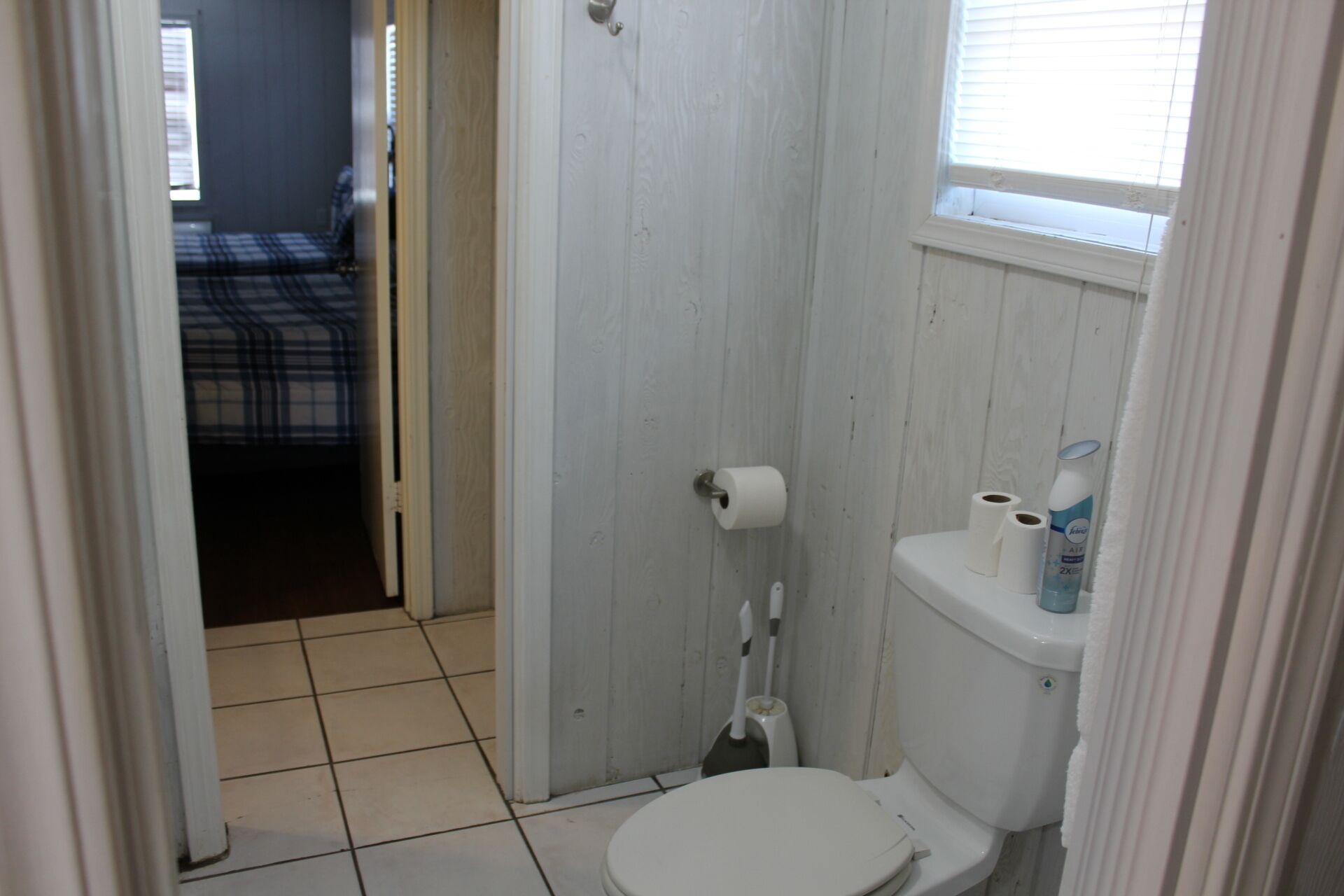 Un baño pequeño y estrecho con un inodoro, un dispensador de papel higiénico y una ventana.