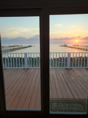A wooden deck with a railing, overlooking a calm body of water and a pier extending into the distance. - 700 North Shore -Grand 4 Bedroom House, Great Views with a 500' lighted pier. (Port Mansfield)