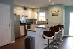 A modern kitchen with white cabinets, a stainless steel refrigerator, a built-in oven, and a large island with bar stools.