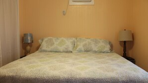 Un lit recouvert d’une couvre-lit à motifs floraux, deux lampes de chevet et une bouche d’aération fixée au mur.
