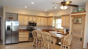 A kitchen with wooden cabinets, stainless steel appliances, a bar area with stools, and a ceiling fan. - 311 Beach - Gorgeous, Brand New Home! Stunning Home with Private Pool! (Port Mansfield)