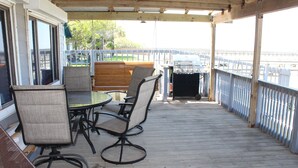 An outdoor deck with a table and chairs, a grill, and a view of the water. - 200 North Shore - Cozy Waterfront Cottage! Excellent Fishing! (Port Mansfield)