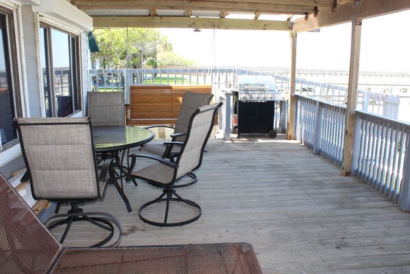 An outdoor deck with a table and chairs, a grill, and a view of the water.