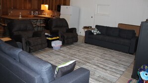 A living room with a sofa set, a coffee table, and a kitchen area with wooden cabinets and a refrigerator. - 200 North Shore - Cozy Waterfront Cottage! Excellent Fishing! (Port Mansfield)