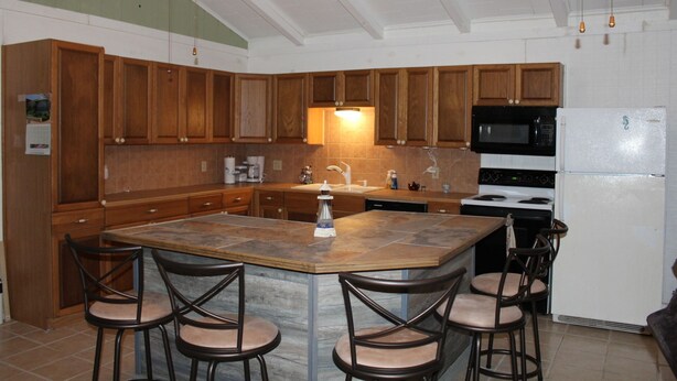 A kitchen with wooden cabinets, a central island with bar stools, a microwave, stove, and refrigerator. - 200 North Shore - Cozy Waterfront Cottage! Excellent Fishing! (Port Mansfield)