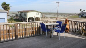 Una terrazza con due sedie blu e un tavolo, con vista su una spiaggia, un molo e una casa con garage.