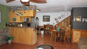 Una cucina con isola in legno, una zona pranzo con tavolo e sedie, una ventola a soffitto e una scala che sale al piano superiore.