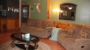 Un soggiorno con un ampio divano marrone, un tavolino in vetro e una testa di cervo appesa al muro.