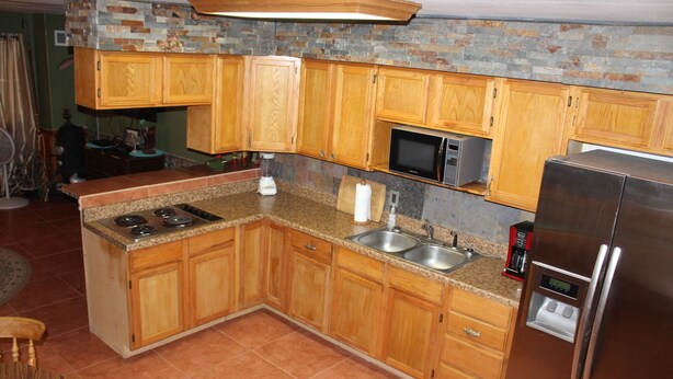 Una cucina con mobili in legno, un forno a microonde, un frigorifero, un fornello e un lavello.
