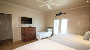 Une chambre avec deux lits, une commode, un ventilateur de plafond et un téléviseur fixé au mur.