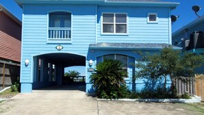 Une maison bleue à deux étages, dotée d’une allée couverte et d’un petit jardin devant.