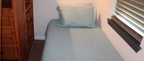 Quarto pequeno com uma cama de solteiro, guarda-roupa de madeira e janela com persianas.