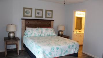 A bedroom with a bed, two bedside tables with lamps, a ceiling fan, and a bathroom visible through an open door.