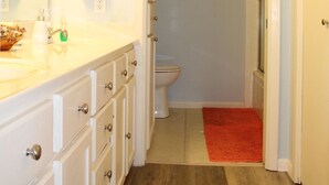A bathroom with a white sink, mirror, and a red bath mat leading to a shower area. - Pelican Point #10 - Beautiful Complex, Gorgeous Sunrises & Easy Access (Port Mansfield)