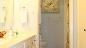 A bathroom with a white sink, mirror, and a red bath mat leading to a shower area.