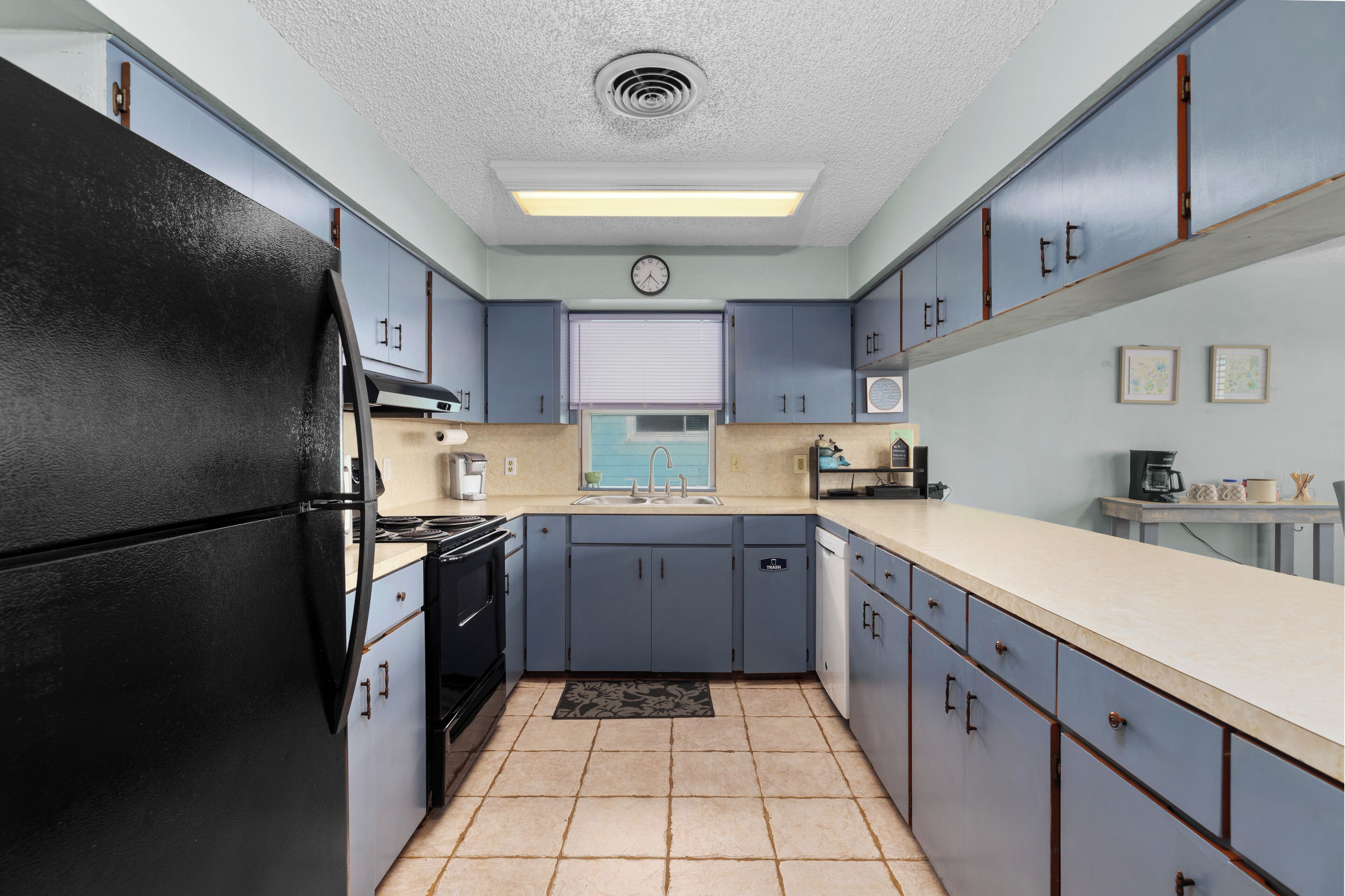 Una cocina con armarios azul claro, un refrigerador negro, un lavamanos y un reloj en la pared.