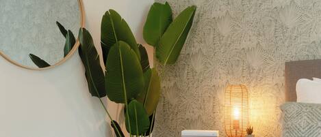 Une chambre à coucher bien rangée, avec une table de chevet, une lampe de chevet, un miroir et une grande plante.