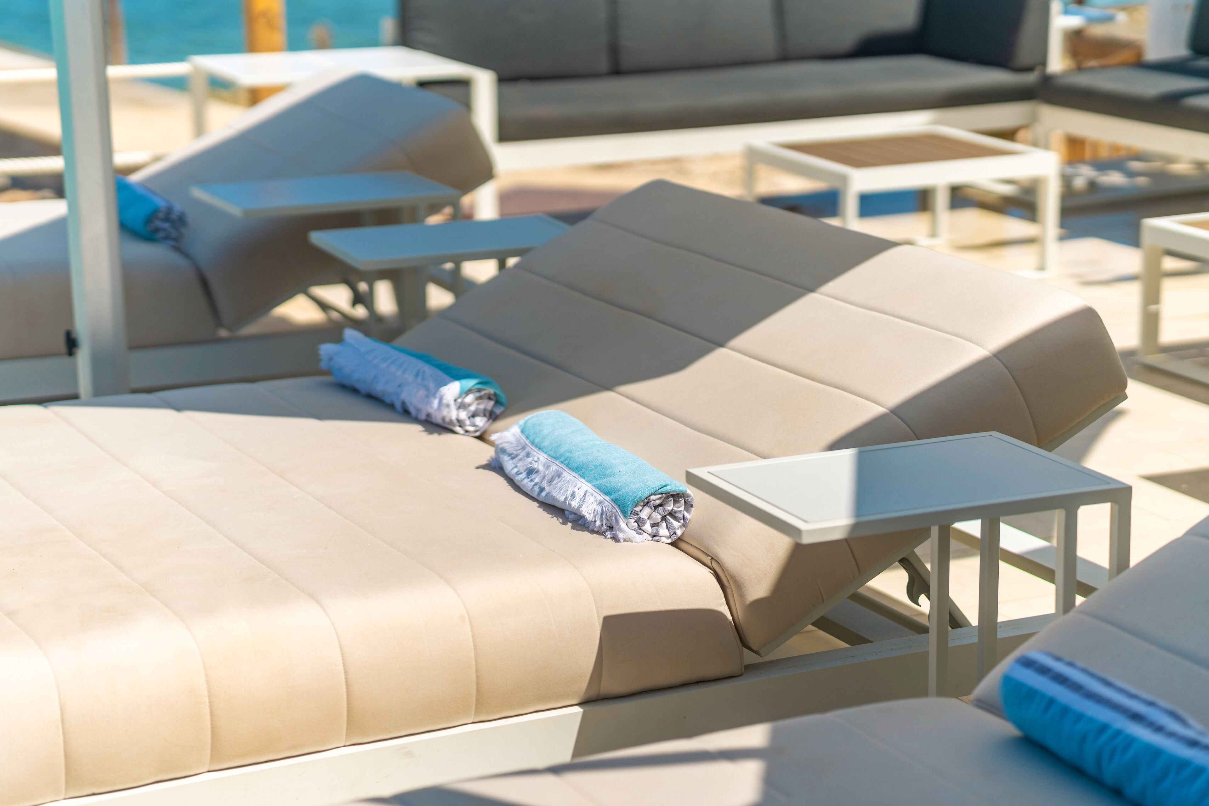 A poolside lounge area with sun loungers, small tables, and a sofa.