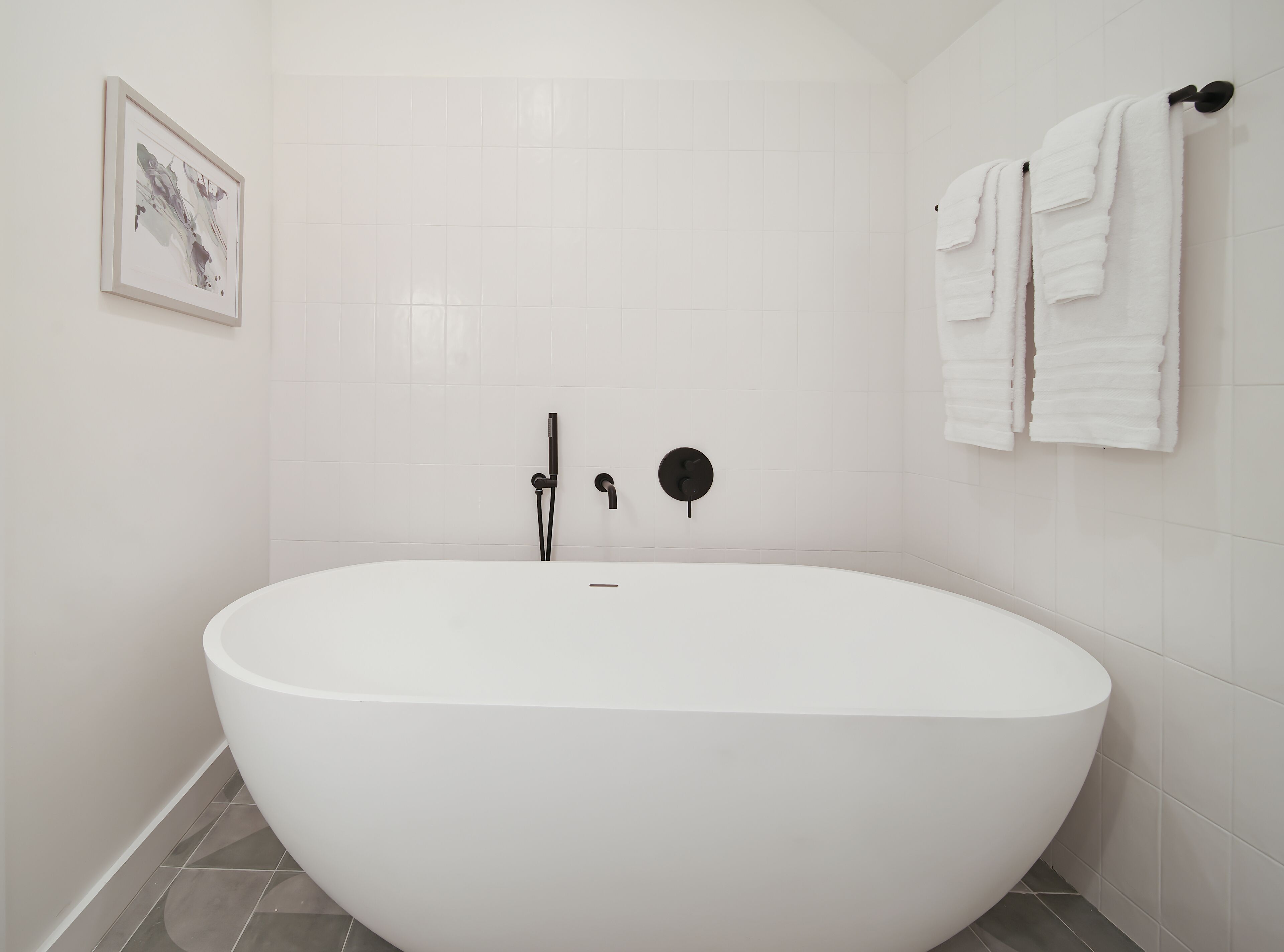 A modern bathroom with a freestanding bathtub, a wall-mounted towel rack, and a framed artwork on the wall.
