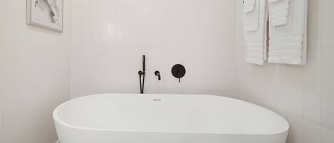 A modern bathroom with a freestanding bathtub, a wall-mounted towel rack, and a framed artwork on the wall.