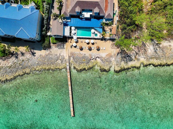 An aerial view of a resort with a swimming pool, sun loungers, and a dock extending into clear turquoise water. - Cobalt Coast Resort (West Bay)