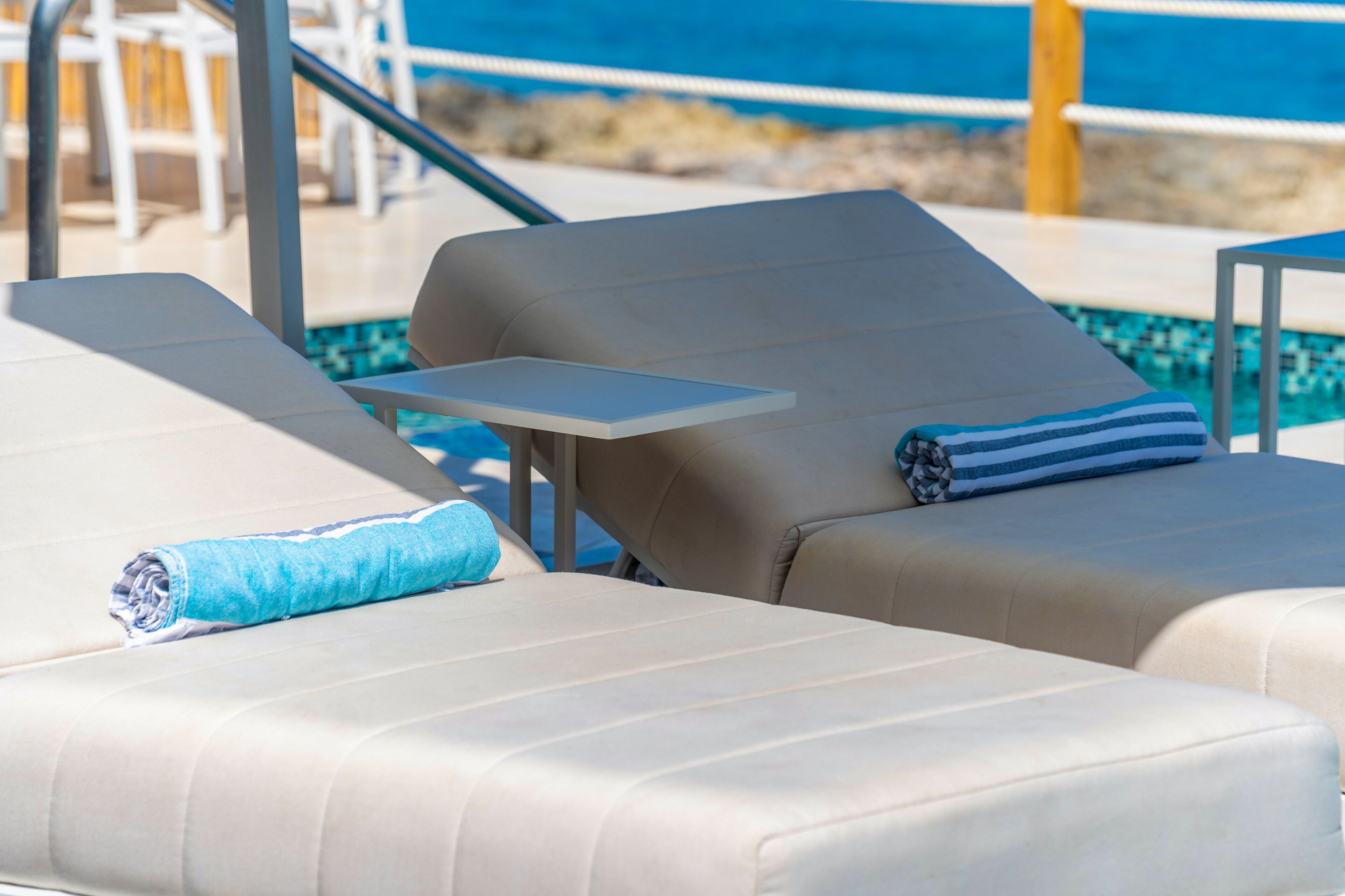 Area relax a bordo piscina con due lettini, ciascuno dotato di un tavolino e un asciugamano.