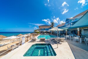 A pool area with a view of the ocean, lounge chairs, and umbrellas. - Cobalt Coast Resort (West Bay)