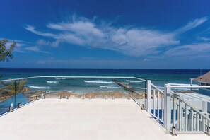 A coastal view from a balcony with a clear sky, ocean waves, and a wooden pier. - Cobalt Coast Resort (West Bay)
