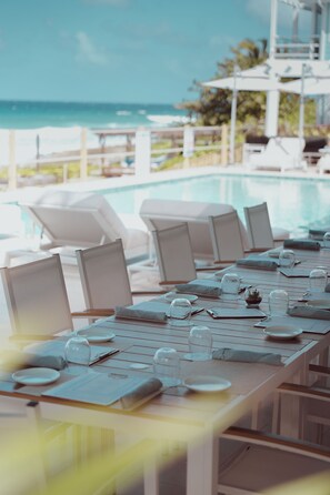 A dining area with a view of the ocean, equipped with white chairs and tables set for a meal. - Cobalt Coast Resort (West Bay)
