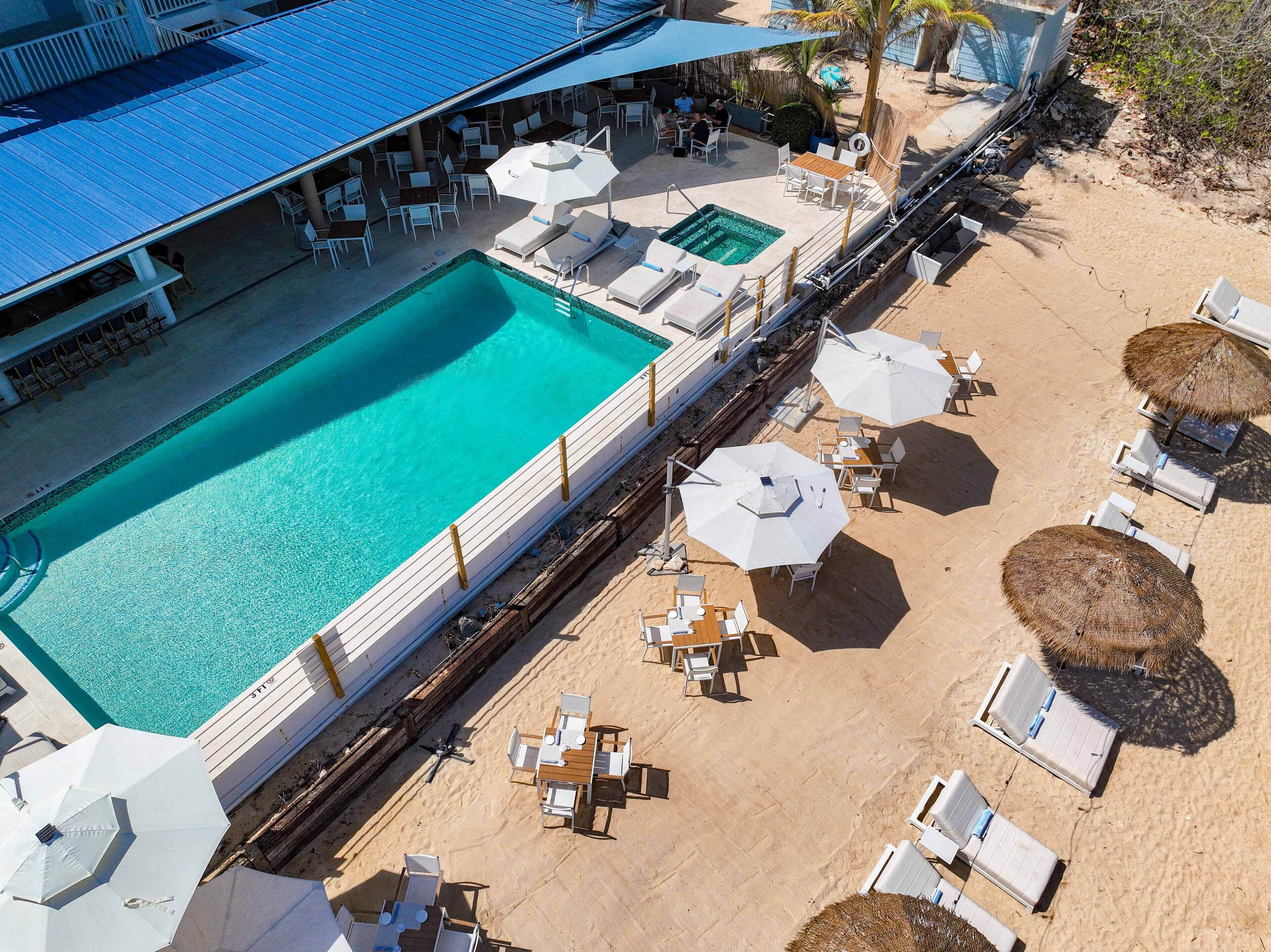 Vue aérienne d’un complexe hôtelier doté d’une piscine, de chaises longues et de parasols.