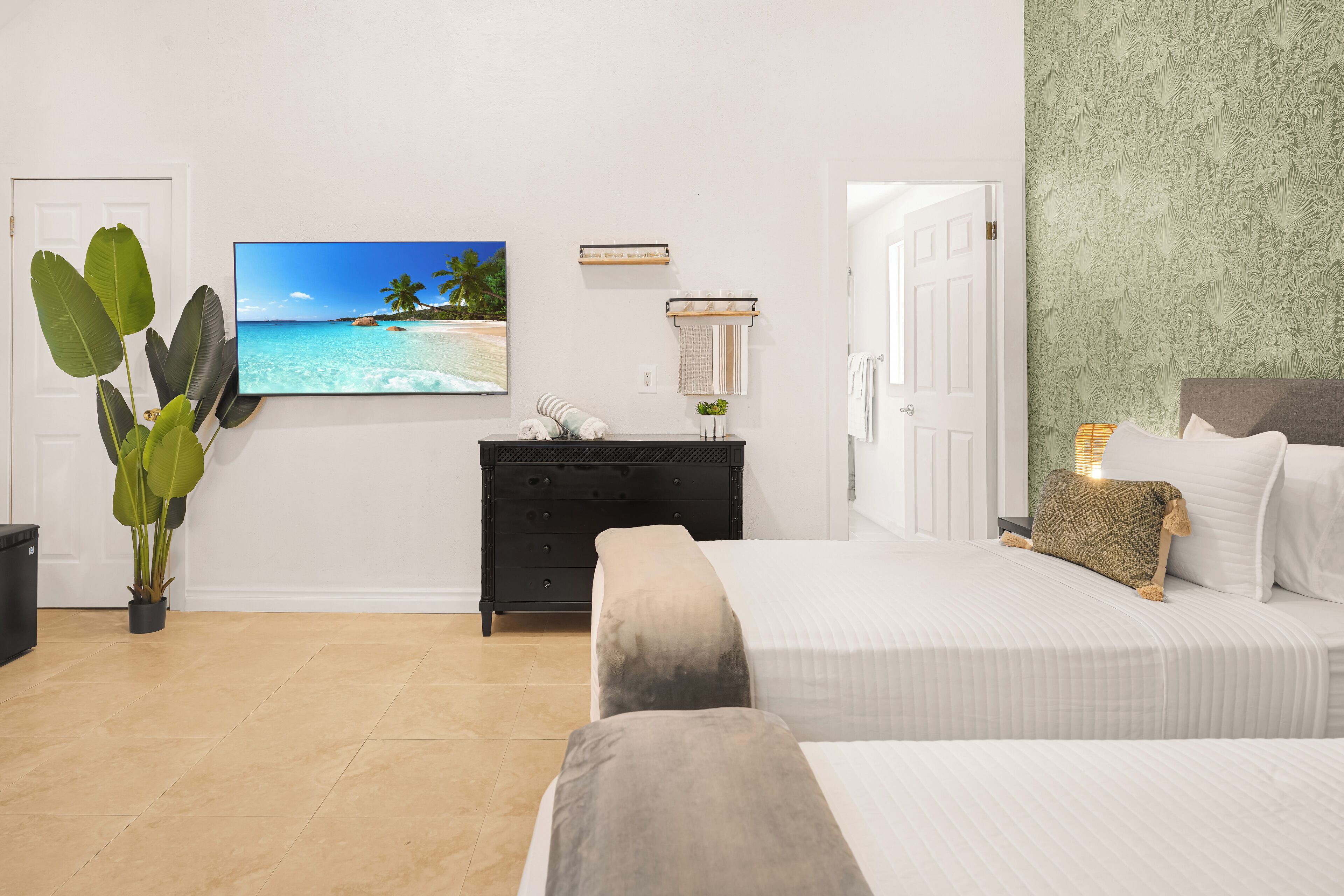 Habitación de hotel con cama, cómoda, planta, pintura de una playa y una puerta.