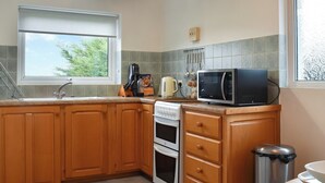 A kitchen with wooden cabinets, a sink, a stove, a microwave, and a window with a view of greenery. - 2 bedroom accommodation in Sockbridge, near Ullswater (Sockbridge, near Ullswater)