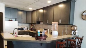 A kitchen with dark cabinets, a large island with bar stools, a refrigerator, and various kitchen appliances. - Loft en Laureles, Coworking y Desayuno Incluido (Medellín)