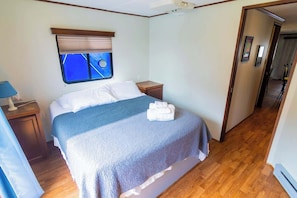 Una camera da letto con un letto, comodini, una finestra con persiane e un corridoio che conduce a un'altra stanza.