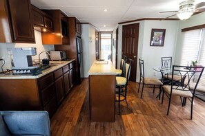 A compact kitchen with wooden cabinets, a central island, and a dining area with chairs and a table.