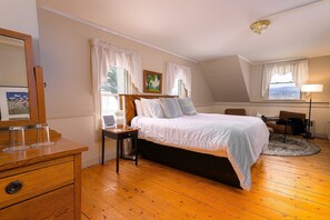 A bedroom with a bed, wooden dresser, bedside table, and a desk with a chair.