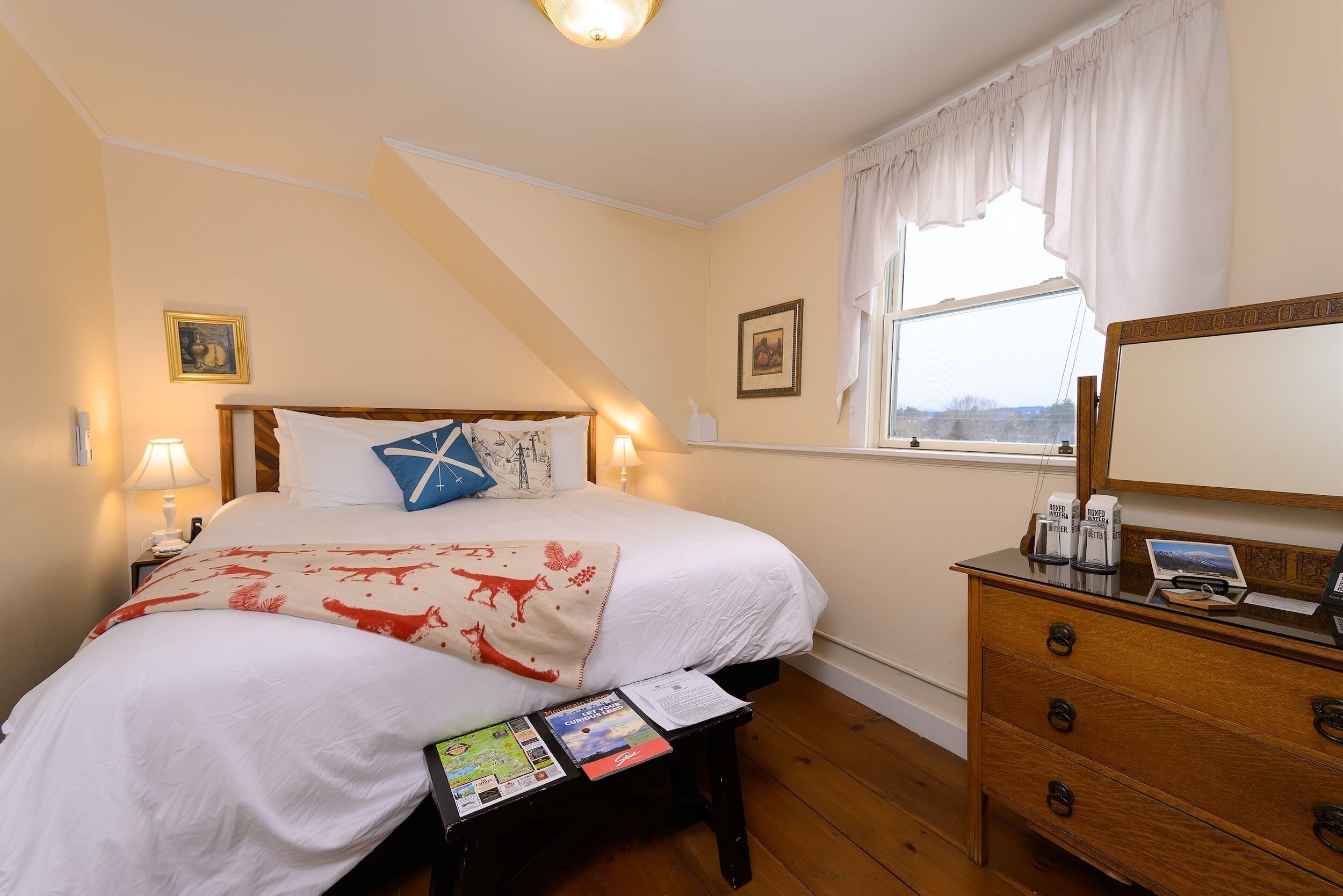 Une chambre à coucher comprenant un lit, une table de chevet, une commode et une fenêtre avec des rideaux.