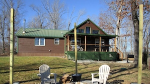A cabin with a green roof, a deck, and a fire pit area with two Adirondack chairs. - Whitetail Ridge (Cadiz)