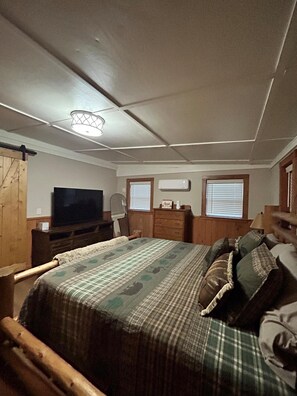Ein Schlafzimmer mit Bett, Fernseher, Kommode und einem Fenster mit Jalousien.