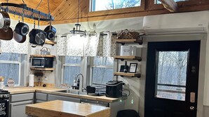 A kitchen with a central island, wooden cabinets, a microwave, and hanging pots. - Whitetail Ridge (Cadiz)