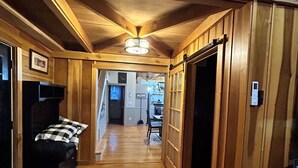 A wooden interior with a hallway leading to a dining area, a bed, and a thermostat on the wall. - Whitetail Ridge (Cadiz)