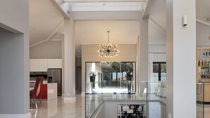 A spacious interior with a modern kitchen, a glass railing overlooking a garden, and a central chandelier.