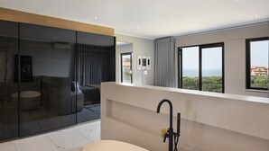 A modern bathroom with a bathtub, a glass-enclosed shower area, and large windows offering a view of the sea.